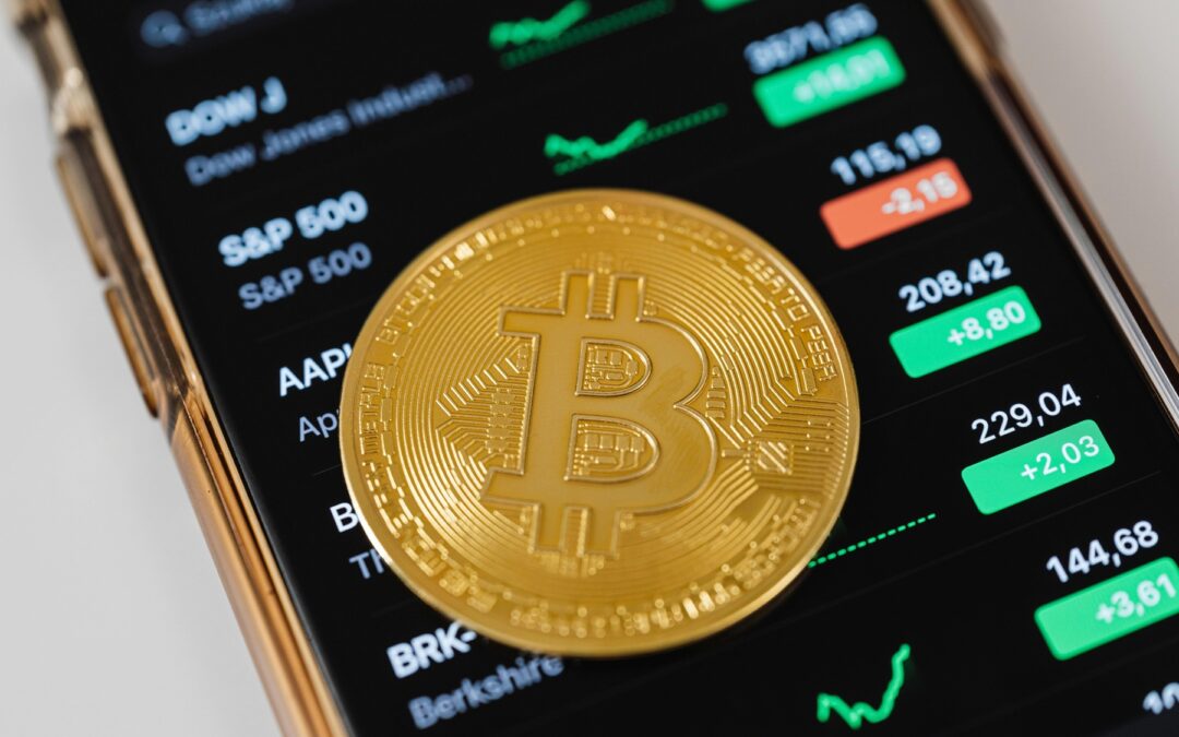 Une pièce dorée de Bitcoin posée sur un smartphone affichant des données boursières