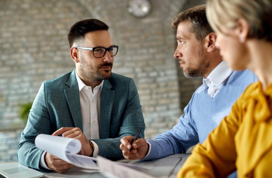 Un conseiller professionnel en veste grise échange avec un client attentif lors d'un rendez-vous dans un bureau moderne