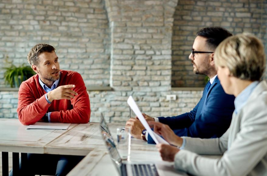 Un échange dynamique entre trois professionnels autour d'une table de travail.