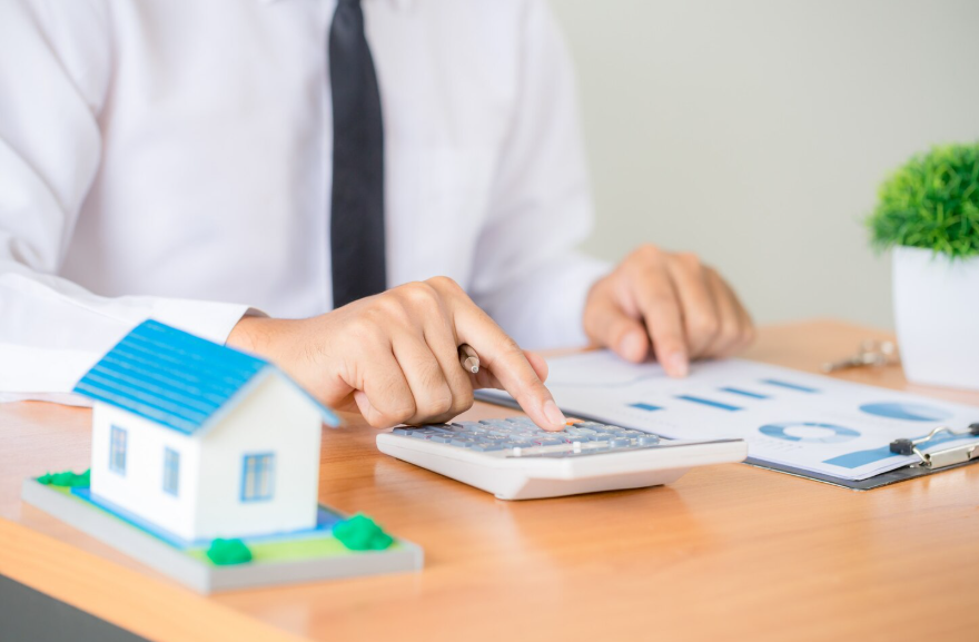 Un professionnel de la finance calcule des données budgétaires à côté d'une maquette de maison sur un bureau.